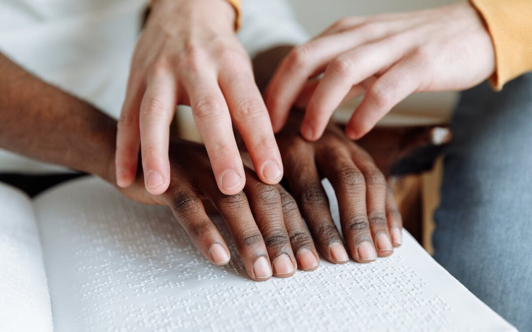 Une personne guide les mains d'une autre personne sur la surface d'un livre en braille.